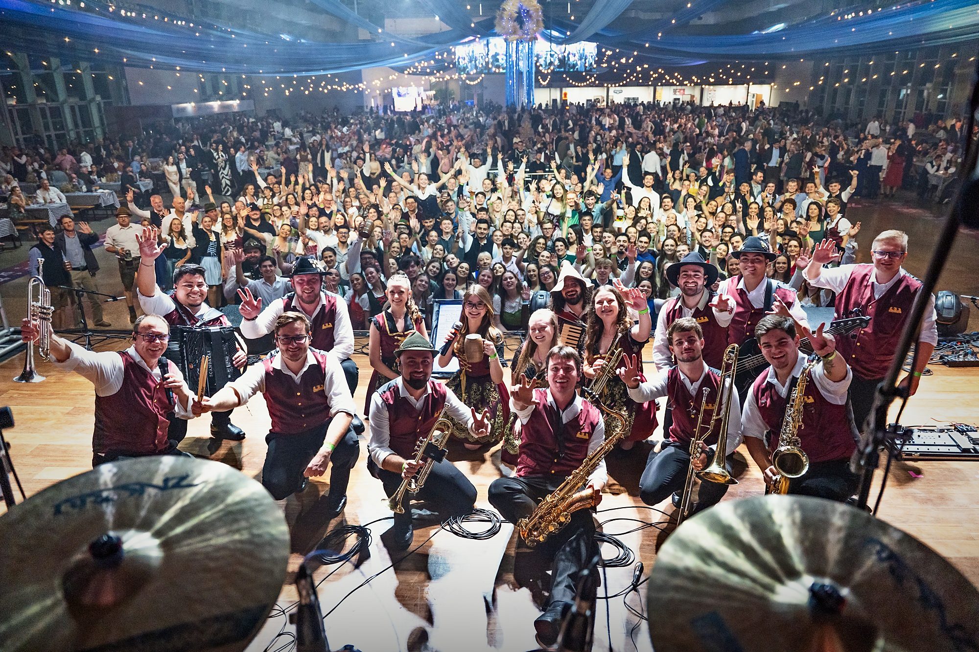 Die Banda Original kniet auf der Bühne und winkt in die Kamera, dahinter der volle Saal.